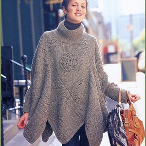 May include: A gray knitted poncho with a large, intricate cable knit design in the center. The poncho has a high neck and a loose fit.