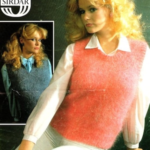 May include: A pink fuzzy knit vest with a V-neck. The vest is worn over a white blouse. The image also shows a woman wearing a blue knit vest with a bow.