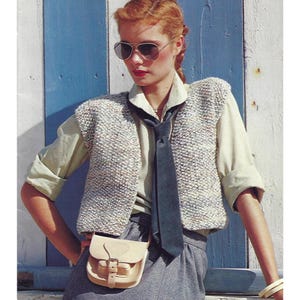 Może przedstawiać: Kobieta w białej, bezrękawnikowej kamizelce z dzianiny w biało-niebieski wzór, białej koszuli z guzikami, ciemnoniebieskim krawacie i jasnobrązowej skórzanej torbie na ramię.