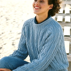 May include: A light blue cable knit sweater with a round neckline. The sweater is made of a soft, comfortable material and has a relaxed fit.