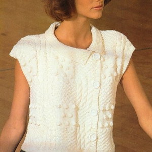 May include: A white knitted sleeveless cardigan with a button closure and a textured pattern. The cardigan has a collar and is made with a soft yarn.