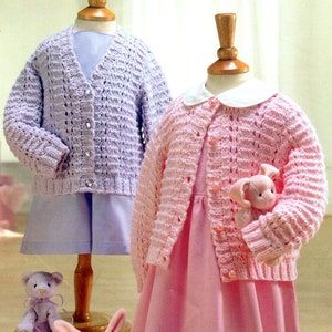 May include: Two knitted cardigans for children, one in lavender and one in pink, with button fastenings and a delicate openwork stitch pattern.