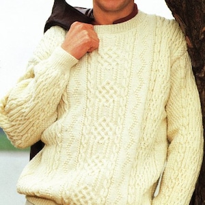 May include: A cream-colored cable knit sweater with a crew neck. The sweater is made of a soft, textured yarn and has a classic, timeless design.