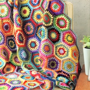 May include: A colourful crocheted blanket with a hexagonal pattern in shades of red, orange, yellow, green, blue, purple, and pink.