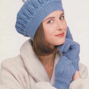 May include: A blue knitted beret with a lacy pattern and matching blue knitted gloves. The beret has a small loop on top.