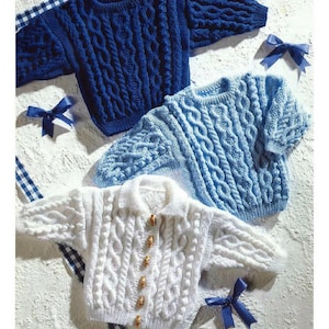 May include: Three cable-knit sweaters in shades of blue and white. The top sweater is a deep navy blue, the middle one is a lighter blue, and the bottom is white. Each sweater has a unique cable pattern. The sweaters are displayed on a textured surface.