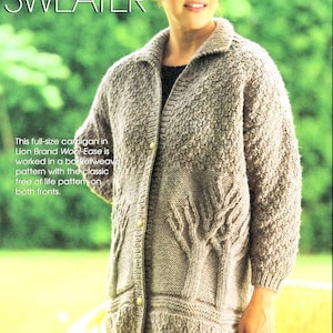Peut inclure: Un cardigan long à manches longues de couleur marron clair avec un motif d'arbre de vie sur le devant. Le pull a un motif en point de panier et est boutonné. Le texte "TREE OF LIFE SWEATER" est en haut.