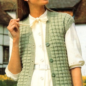 Puede incluir: Un chaleco de punto verde sin mangas con cierre de botones. El chaleco se lleva sobre una camisa blanca de botones con una pajarita.