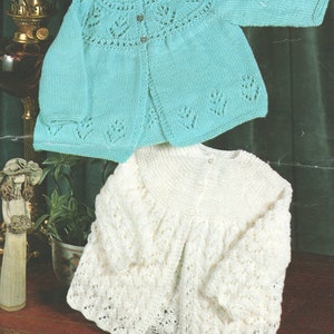 Könnte beinhalten: Zwei gestrickte Baby-Pullover, einer in hellblau mit einem Spitzenmuster und der andere in weiß mit einem zarten Lochmuster.