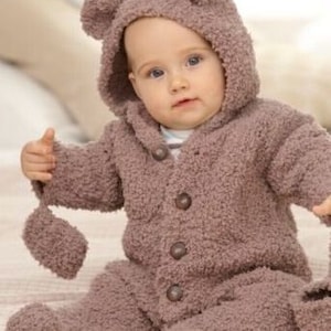 May include: A baby wearing a brown, hooded bear suit with attached mittens and feet. The suit has a button-up front and bear ears on the hood. The text "Birth to 2 years" is visible in the upper right corner.