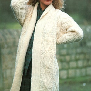 May include: A white knitted cardigan with a cable knit pattern and a shawl collar. The cardigan is open in the front and has long sleeves.