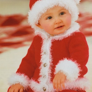 Op de afbeelding: Een baby die een rood gebreid kerstmanpak draagt met witte bontbies. Het pak heeft een knoopsluiting en de baby draagt een bijpassende kerstmanmuts.