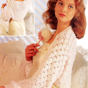 May include: A light pink, open-weave crochet bolero with long sleeves. The bolero is worn over a light-coloured dress. The image also includes a small inset of the bolero from a different angle. The bolero is a delicate, feminine garment.