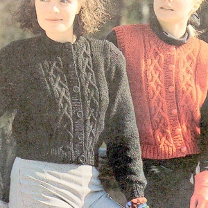 May include: Two women wearing knitted cardigans. The woman on the left is wearing a black cardigan with a cable knit pattern and buttons. The woman on the right is wearing a red cardigan with a cable knit pattern and buttons.