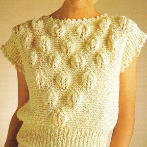 May include: A short-sleeved, light yellow knitted top with a textured pattern of raised leaf-like shapes. The top has a ribbed hem and a crew neck. The overall style is vintage and handmade, suitable for casual wear.
