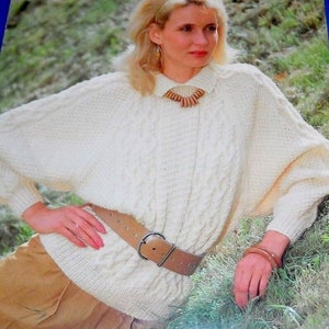 May include: A white knitted sweater with a cable knit pattern and a brown leather belt. The sweater has a wide, loose fit and long sleeves.