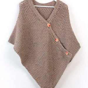 May include: A brown knitted poncho with a v-neck and a diagonal button closure. The poncho has a speckled pattern and is made with a soft yarn.