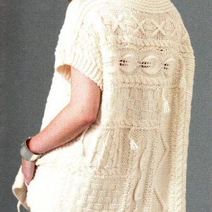 以下が含まれることがあります： ケーブル編みのデザインとゆったりとしたフィット感のある白いニットセーター。セーターは半袖で、丸首です。