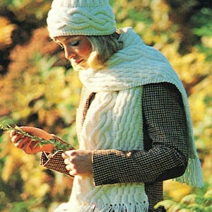 May include: A white knitted hat and scarf set with a cable knit pattern. The hat has a folded brim and the scarf has fringe.
