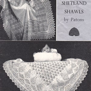 May include: A white crocheted baby shawl with a delicate lace pattern. The shawl is laid out on a surface with a baby lying on a pillow in the background. The pattern number is IO85-6 and the text reads "Two 2-ply Shetland Shawls by Patons".