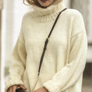 May include: A white knitted turtleneck sweater with a brown leather shoulder bag. The sweater has a loose fit and long sleeves.