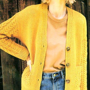 May include: A yellow knitted cardigan with a cable knit pattern on the sleeves and pockets. The cardigan has a V-neck and button closure.