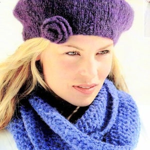 May include: A purple knitted beret with a flower embellishment. The beret is worn by a person with blonde hair and a blue knitted scarf.