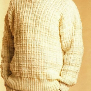 Könnte beinhalten: Ein weißer Strickpullover mit einem strukturierten Muster. Der Pullover hat einen Rundhalsausschnitt und lange Ärmel.