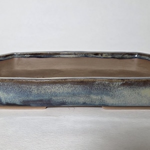 May include: A rectangular ceramic bonsai pot with an elongated shape and beveled corners. The exterior features a reactive glaze with blended tones of deep blue, slate gray, and hints of cream, while the interior has a smooth, light tan finish.