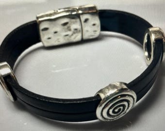 May include: A black leather bracelet with silver metal accents. The bracelet has a magnetic clasp and a spiral design on one of the accents.