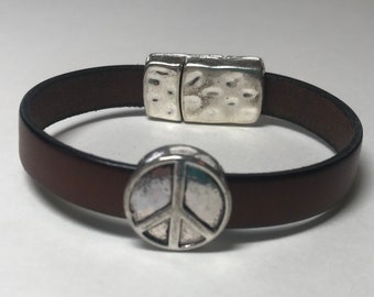 May include: A brown leather bracelet with a silver peace sign charm and a magnetic clasp.