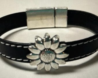May include: A black leather bracelet with a silver sunflower charm and a magnetic clasp.