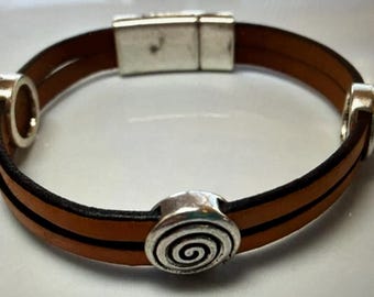 May include: A brown leather bracelet with a silver magnetic clasp and a silver spiral charm.