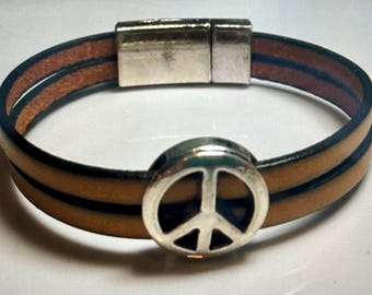 May include: A brown leather bracelet with a silver peace sign charm. The bracelet has a magnetic clasp.