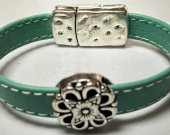 May include: A teal leather bracelet with a silver magnetic clasp and a silver flower charm.