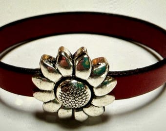 May include: A red leather bracelet with a silver sunflower charm.