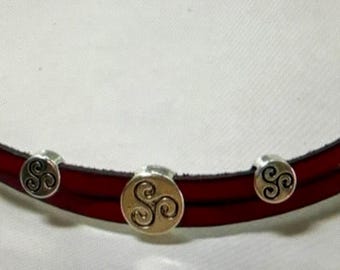 May include: A red leather bracelet with silver-colored accents. The bracelet features three silver-colored circular charms with a Celtic spiral design and silver-colored clasps. The bracelet is curved and appears to be made of two layers of leather.