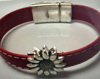 May include: Red leather bracelet with a silver sunflower charm. The bracelet has a magnetic clasp and white stitching along the edges. The sunflower charm is detailed with individual petals and a textured center.