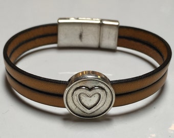 May include: A brown leather bracelet with a silver heart charm. The bracelet has a magnetic clasp.