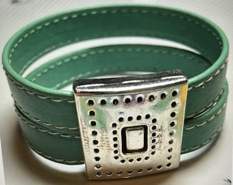 May include: A double-wrap green leather bracelet with a silver-toned clasp featuring a decorative pattern of small circles.