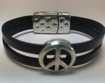 May include: A black leather bracelet with a silver peace sign charm and a magnetic clasp.