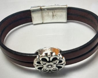 May include: A brown leather bracelet with a silver magnetic clasp and a silver flower charm.