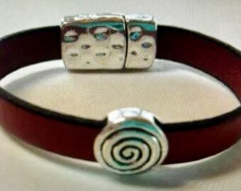 May include: A red leather bracelet with a silver clasp and a silver charm with a spiral design.