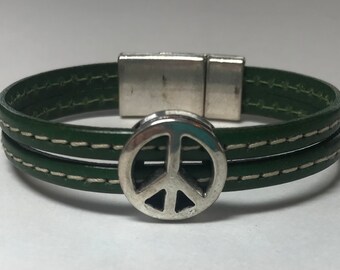 May include: A green leather bracelet with a silver peace sign charm and a magnetic clasp.