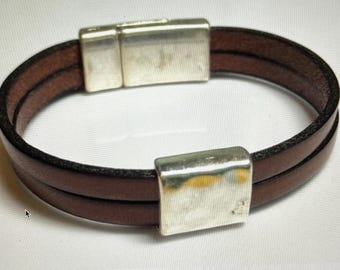 May include: A brown leather bracelet with a silver magnetic clasp. The bracelet is double-layered and has a smooth finish.