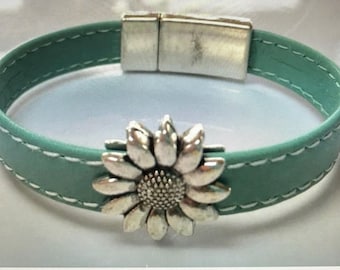 May include: A teal leather bracelet with a magnetic clasp and a silver sunflower charm.