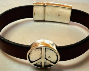 May include: A brown leather bracelet with a silver magnetic clasp and a silver peace sign charm.