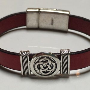 May include: A red leather bracelet with a silver magnetic clasp and a silver Celtic knot design.