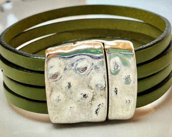 May include: A green leather wrap bracelet with a silver clasp. The clasp has a hammered texture.