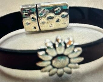 May include: A black leather bracelet with a silver magnetic clasp and a silver sunflower charm.